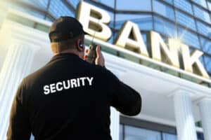 Addetto alla vigilanza fuori all'entrata di una banca mentre comunica con il walkie talkie Addetto alla vigilanza fuori all'entrata di una banca mentre comunica con il walkie talkie
